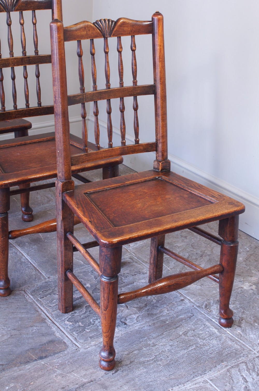 A set of six dark oak country dining chairs featuring carved shell crest rails, spindle backs, turned legs, and solid wood panel seats. View VI