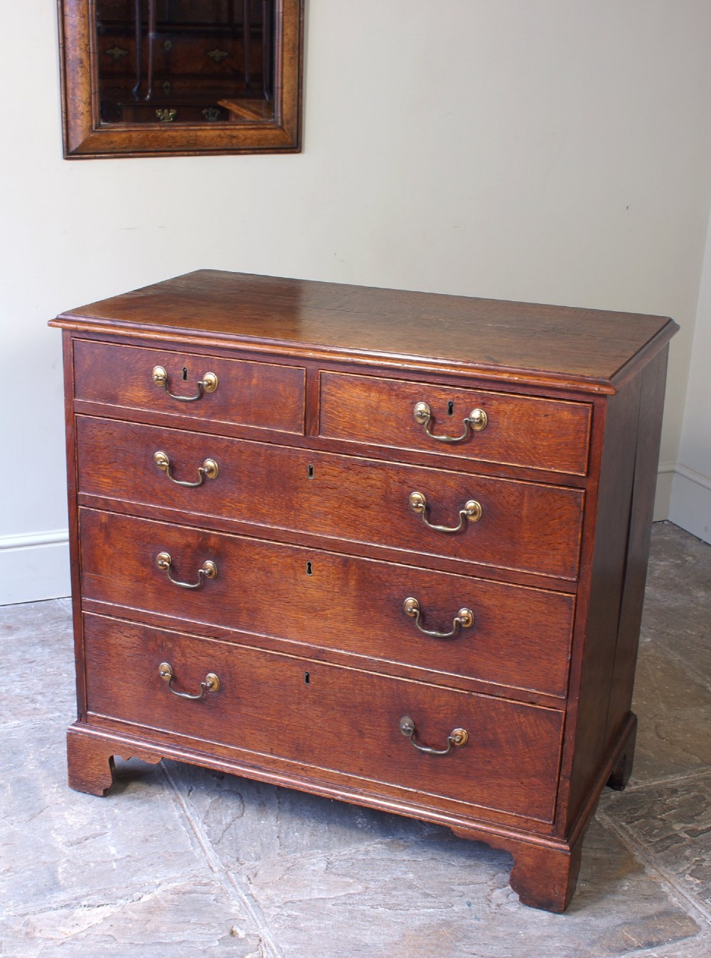 A Georgian oak chest of drawers featuring two short over three long graduated drawers with brass swan-neck handles and bracket feet. View II