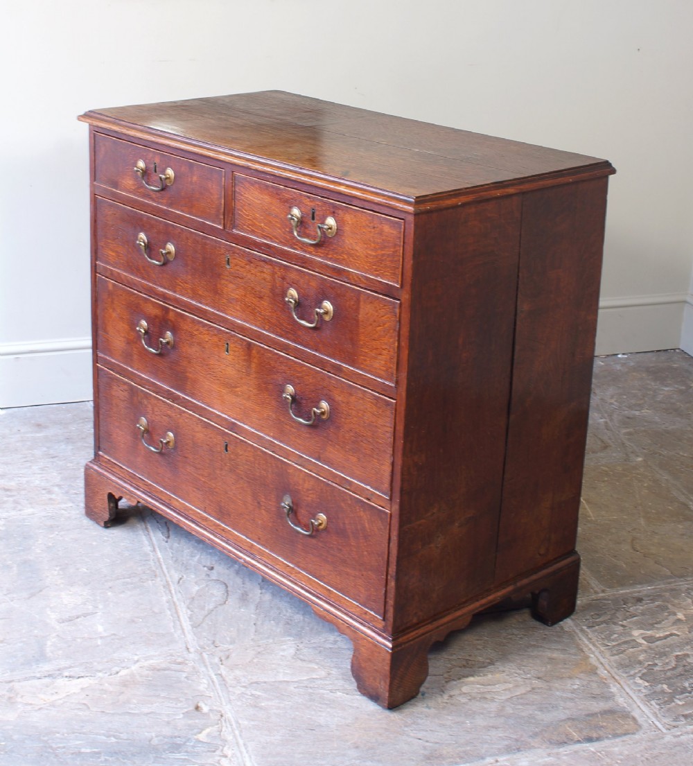 A Georgian oak chest of drawers featuring two short over three long graduated drawers with brass swan-neck handles and bracket feet.