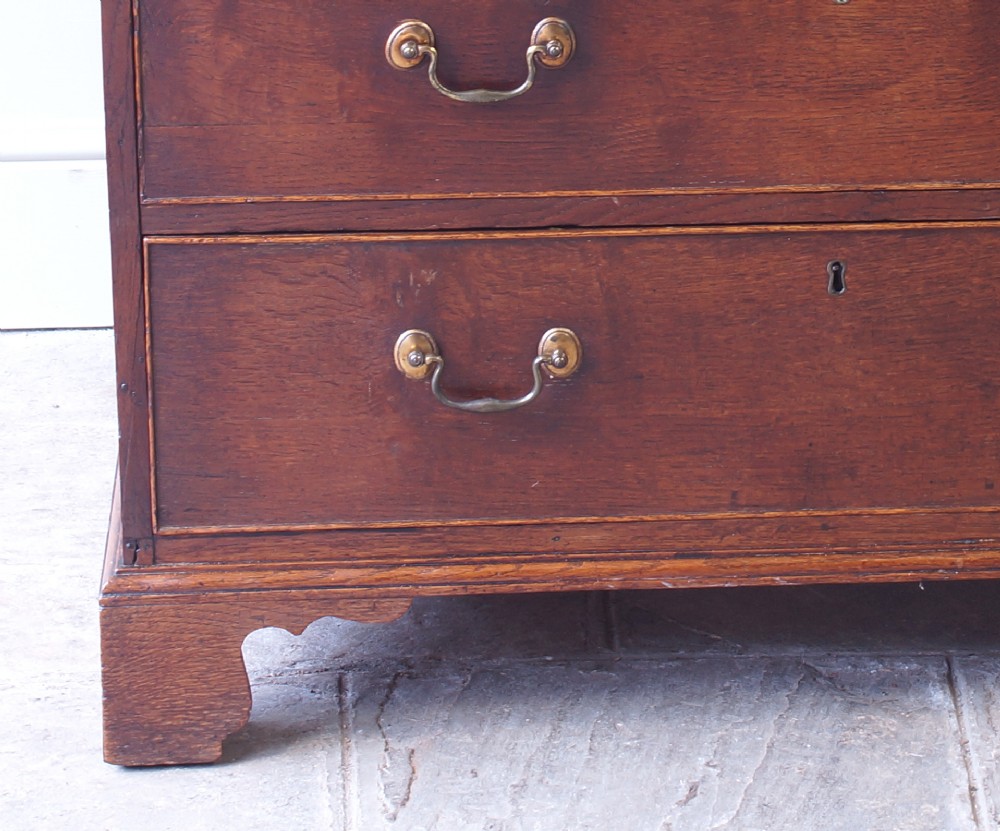 A Georgian oak chest of drawers featuring two short over three long graduated drawers with brass swan-neck handles and bracket feet. View VIII