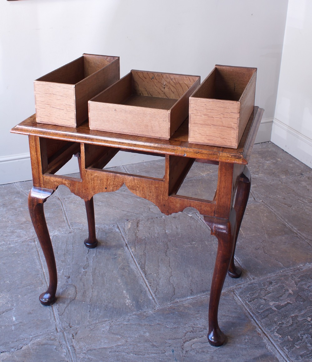 An early 18th-century walnut lowboy table with three drawers, brass ring pull handles, a scalloped apron, and cabriole legs ending in pad feet. View V