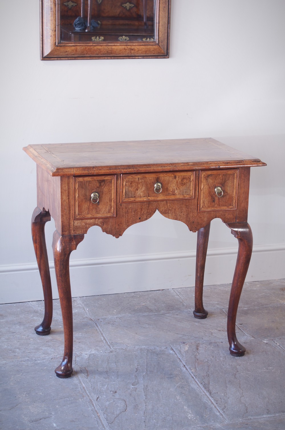 An early 18th-century walnut lowboy table with three drawers, brass ring pull handles, a scalloped apron, and cabriole legs ending in pad feet. View II