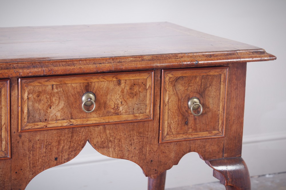 An early 18th-century walnut lowboy table with three drawers, brass ring pull handles, a scalloped apron, and cabriole legs ending in pad feet. View X