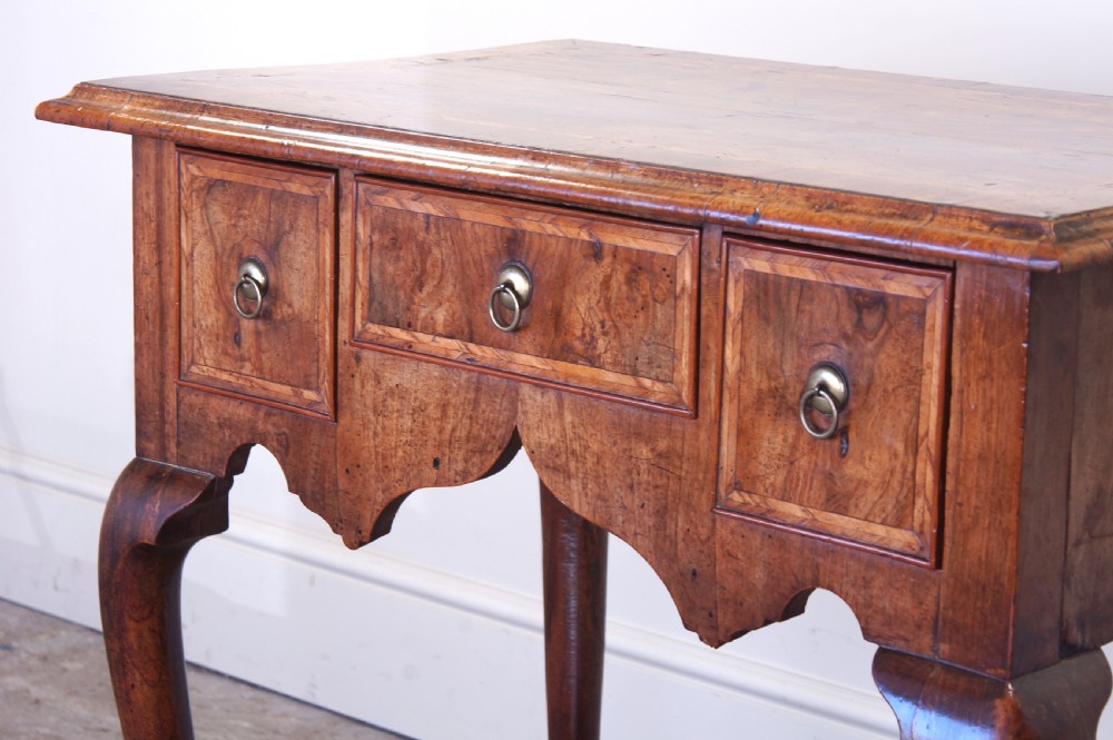 An early 18th-century walnut lowboy table with three drawers, brass ring pull handles, a scalloped apron, and cabriole legs ending in pad feet. View XIV
