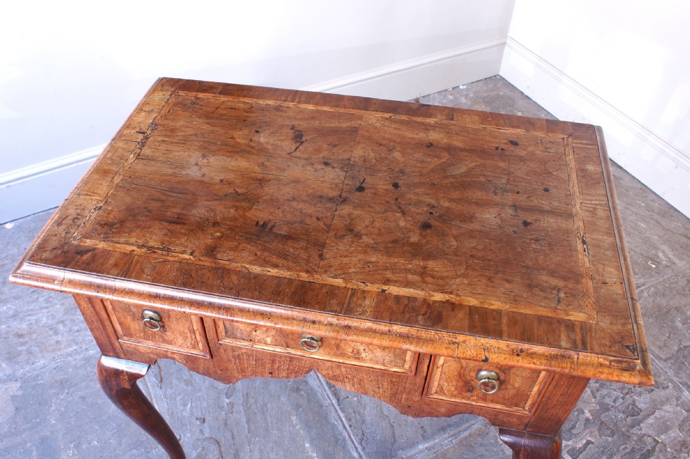 An early 18th-century walnut lowboy table with three drawers, brass ring pull handles, a scalloped apron, and cabriole legs ending in pad feet. View XV