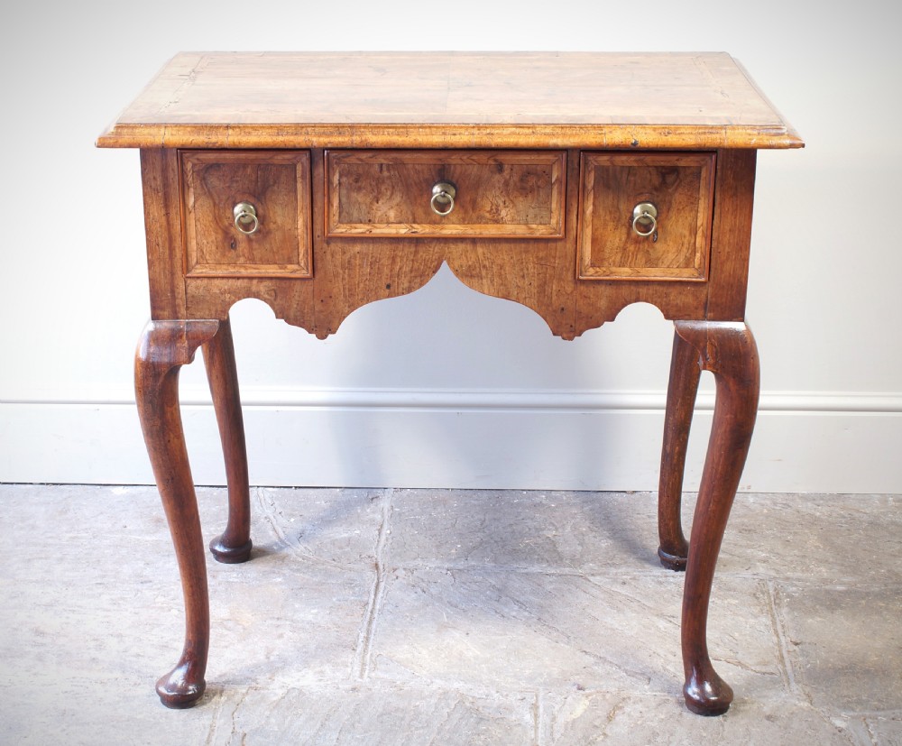 An early 18th-century walnut lowboy table with three drawers, brass ring pull handles, a scalloped apron, and cabriole legs ending in pad feet. View XVII