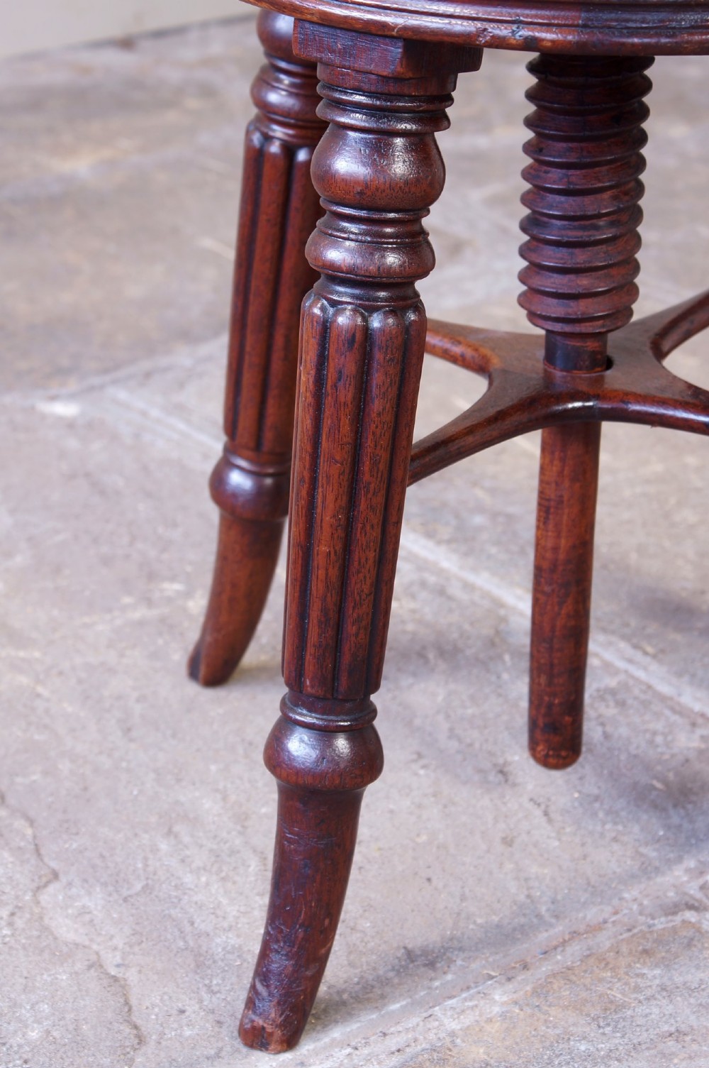 A Regency mahogany revolving piano stool featuring a circular floral needlepoint cushion, central wooden screw mechanism, and fluted turned legs. View II