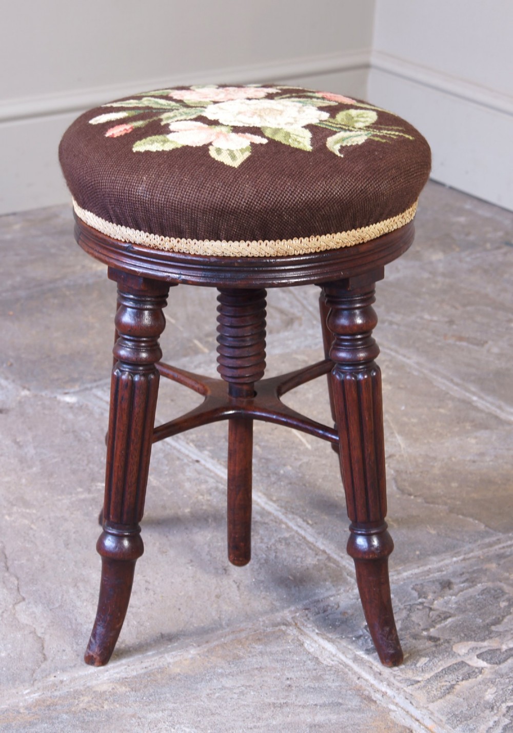 A Regency mahogany revolving piano stool featuring a circular floral needlepoint cushion, central wooden screw mechanism, and fluted turned legs. View III