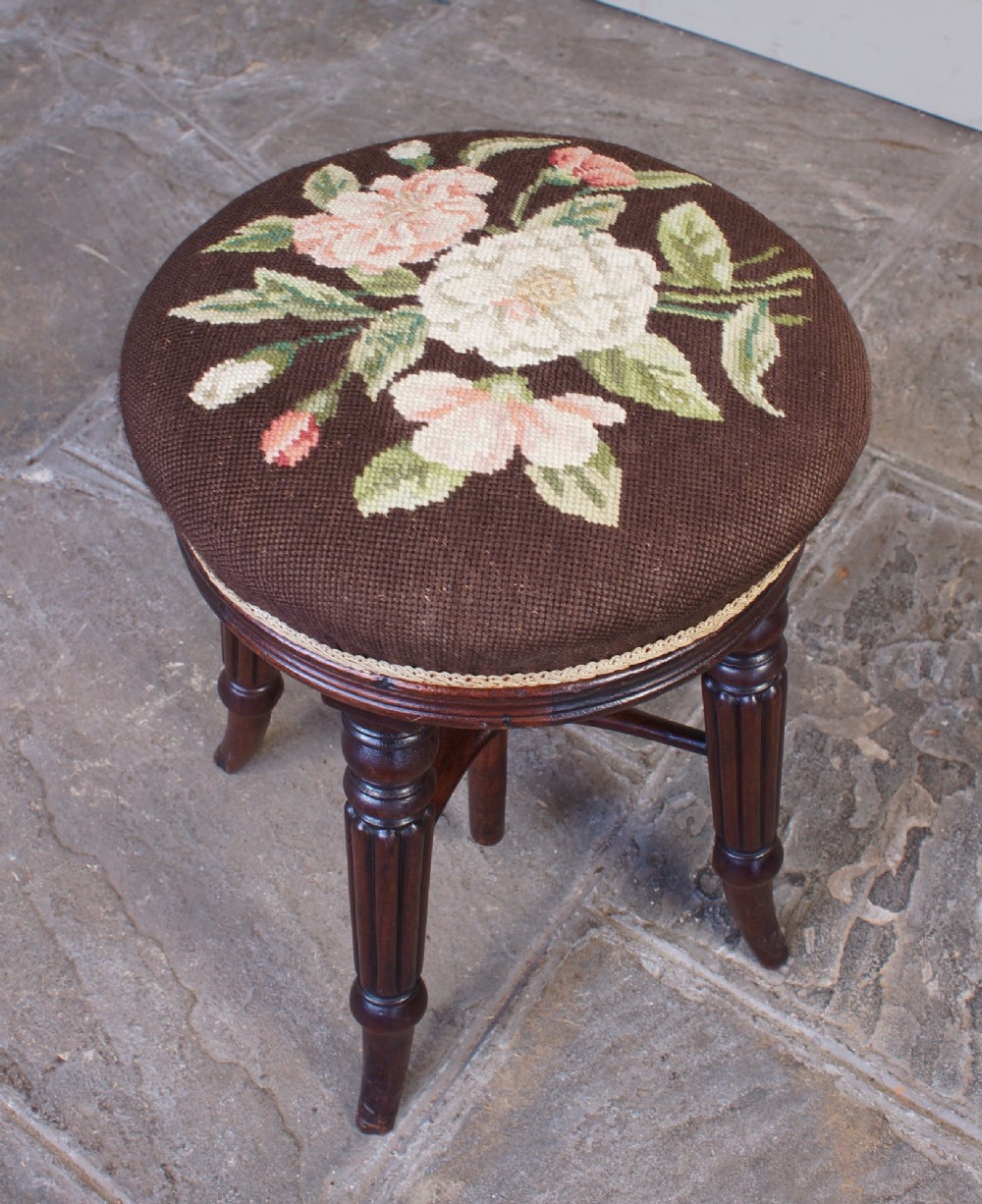A Regency mahogany revolving piano stool featuring a circular floral needlepoint cushion, central wooden screw mechanism, and fluted turned legs. View VII