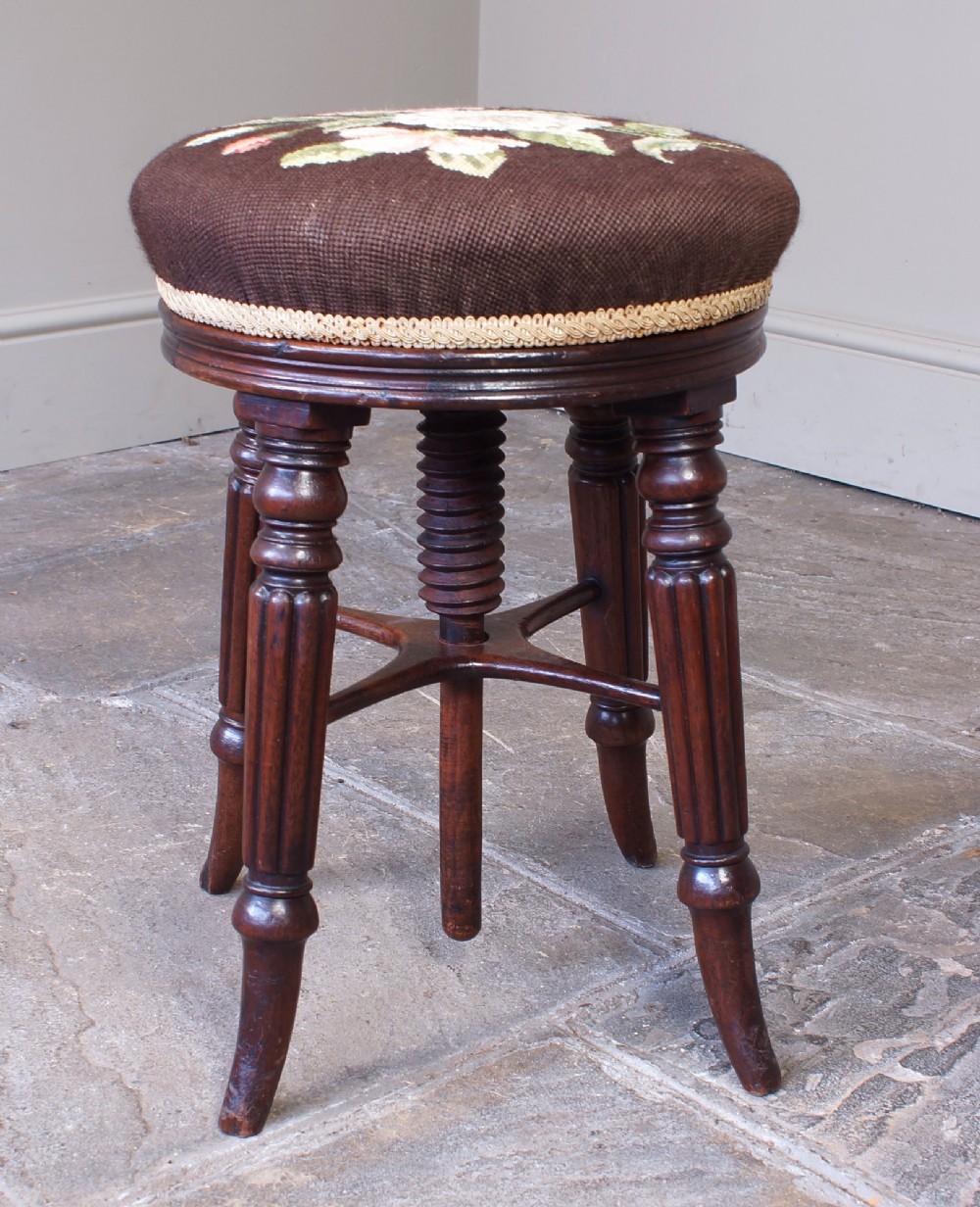 A Regency mahogany revolving piano stool featuring a circular floral needlepoint cushion, central wooden screw mechanism, and fluted turned legs. View VIII