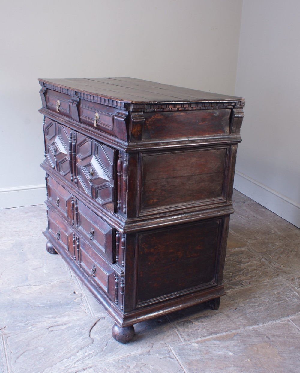 A 17th-century Charles II dark oak chest of drawers featuring geometric mitred panels, turned split spindles, brass drop handles, and bun feet. View II