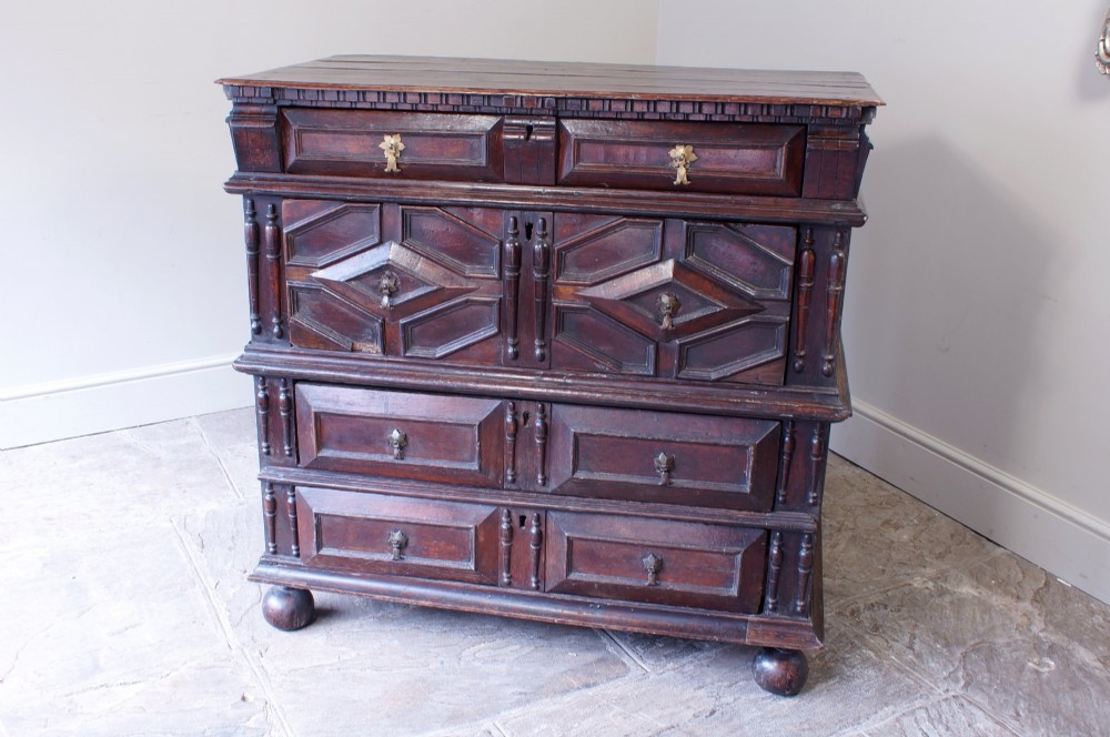 A 17th-century Charles II dark oak chest of drawers featuring geometric mitred panels, turned split spindles, brass drop handles, and bun feet. View III
