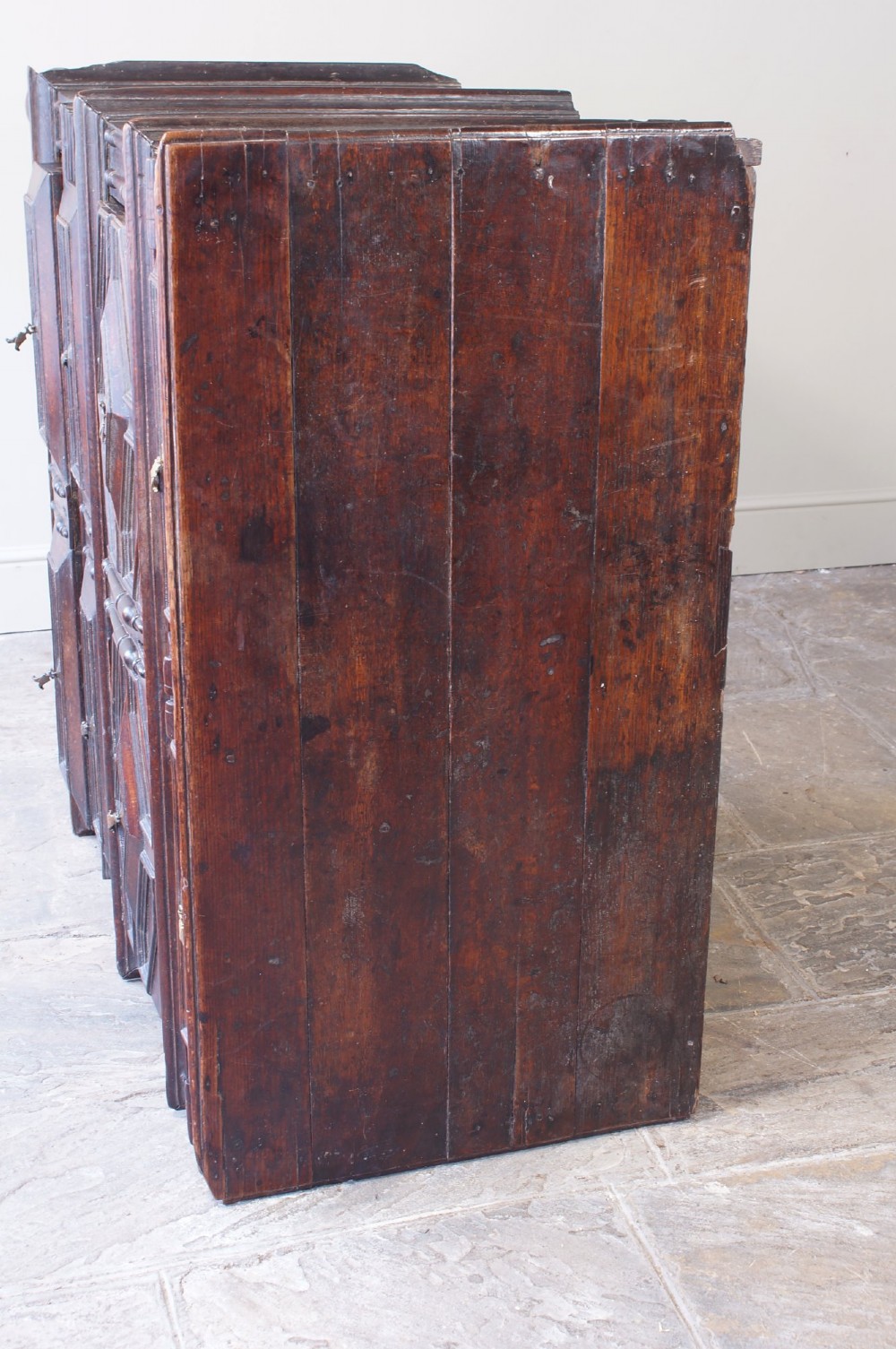 A 17th-century Charles II dark oak chest of drawers featuring geometric mitred panels, turned split spindles, brass drop handles, and bun feet. View V