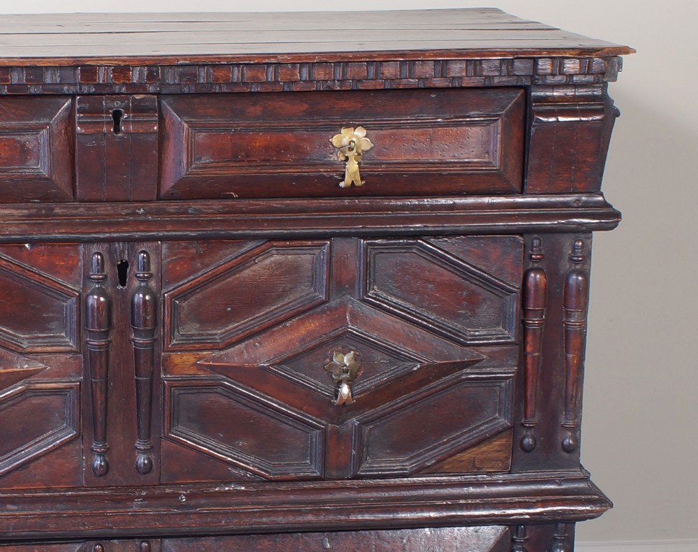 A 17th-century Charles II dark oak chest of drawers featuring geometric mitred panels, turned split spindles, brass drop handles, and bun feet. View IX