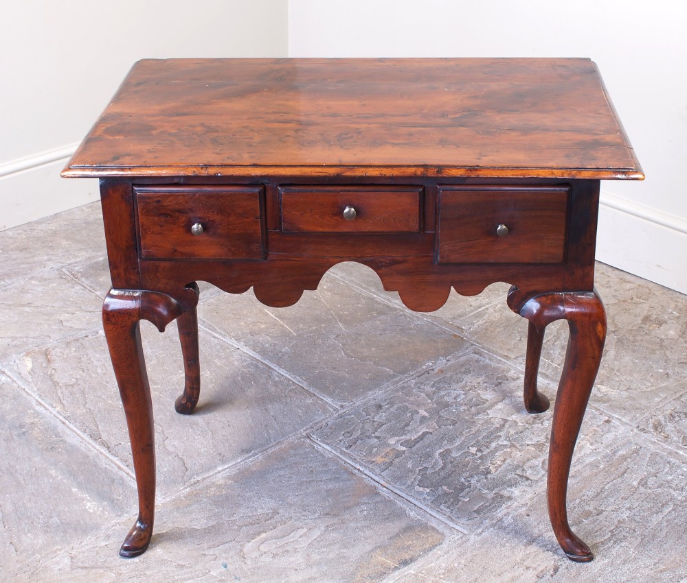 An 18th-century yew wood lowboy table featuring three drawers, a shaped scalloped apron, metal knob handles, and cabriole legs. View II