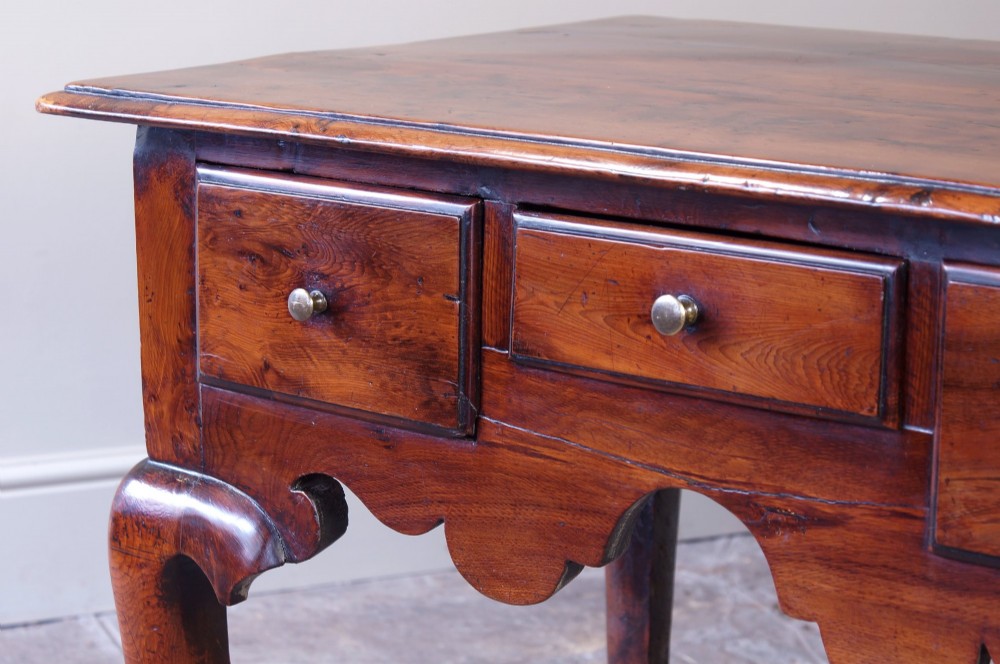 An 18th-century yew wood lowboy table featuring three drawers, a shaped scalloped apron, metal knob handles, and cabriole legs. View VI