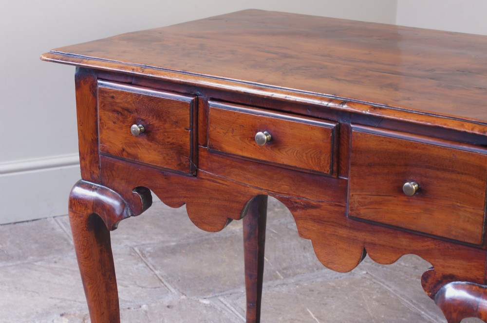 An 18th-century yew wood lowboy table featuring three drawers, a shaped scalloped apron, metal knob handles, and cabriole legs. View XI