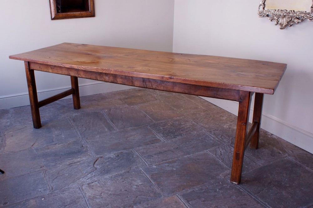 A long nineteenth-century elm farmhouse dining table with a thick plank top, straight legs, and side stretchers.