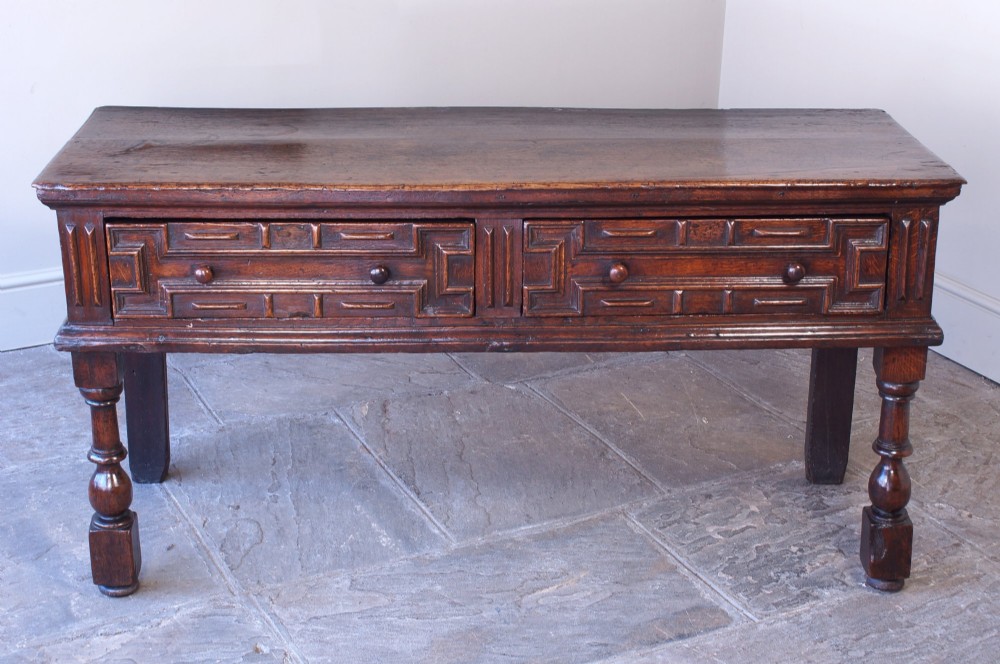 A 17th-century dark oak dresser base featuring geometric mitred mouldings across two drawers, turned front legs, and wooden drawer knobs. View III