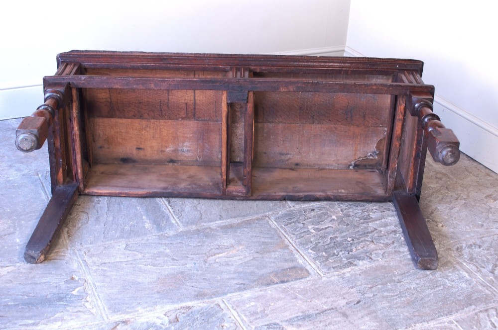 A 17th-century dark oak dresser base featuring geometric mitred mouldings across two drawers, turned front legs, and wooden drawer knobs. View VI