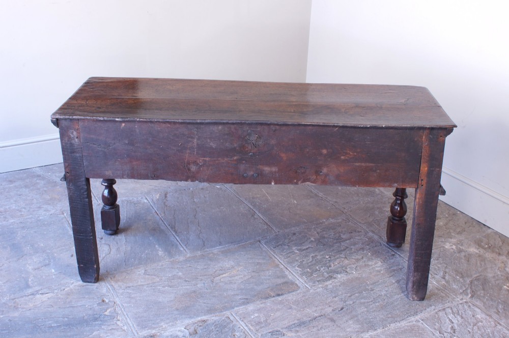 A 17th-century dark oak dresser base featuring geometric mitred mouldings across two drawers, turned front legs, and wooden drawer knobs. View VII