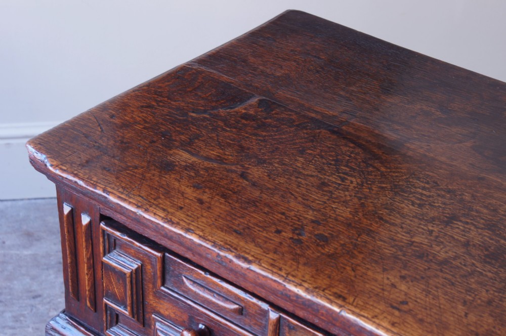 A 17th-century dark oak dresser base featuring geometric mitred mouldings across two drawers, turned front legs, and wooden drawer knobs. View X