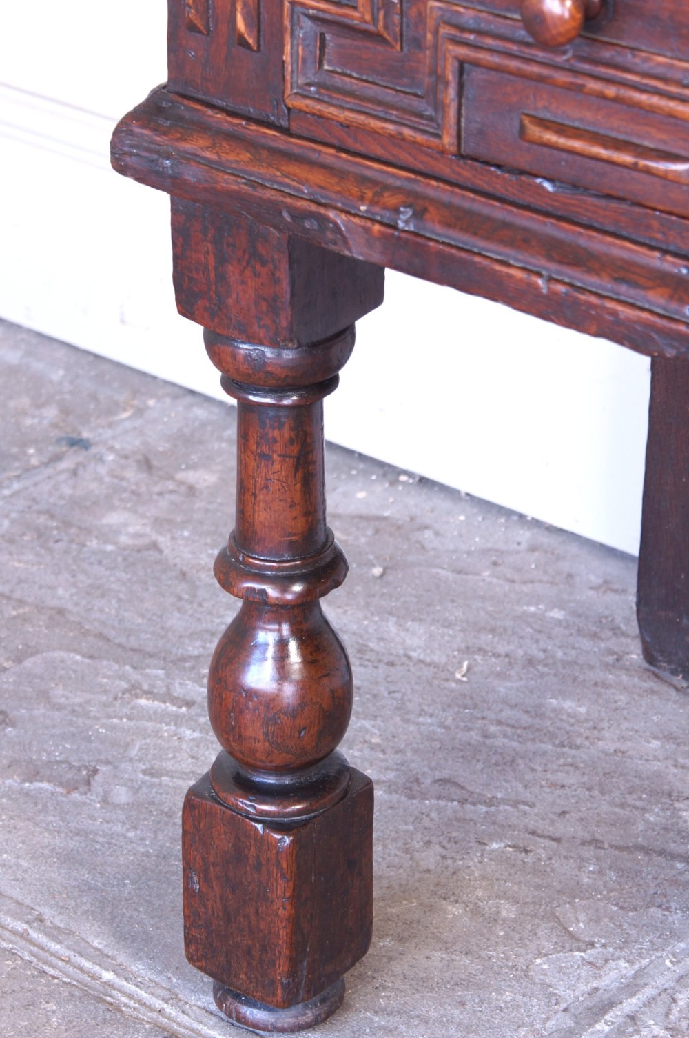 A 17th-century dark oak dresser base featuring geometric mitred mouldings across two drawers, turned front legs, and wooden drawer knobs. View XIV