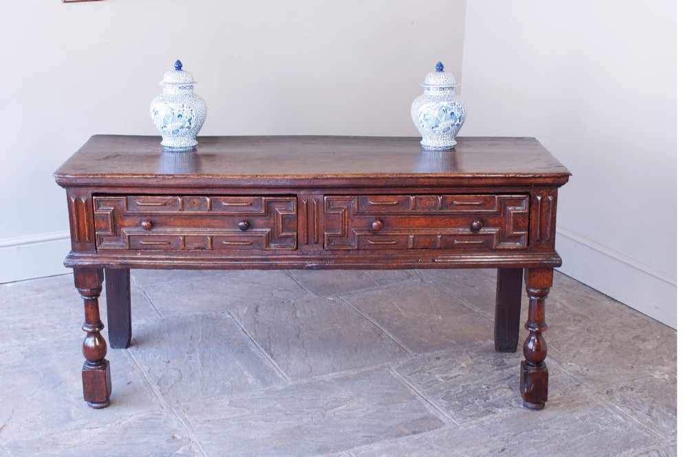 A 17th-century dark oak dresser base featuring geometric mitred mouldings across two drawers, turned front legs, and wooden drawer knobs. View II