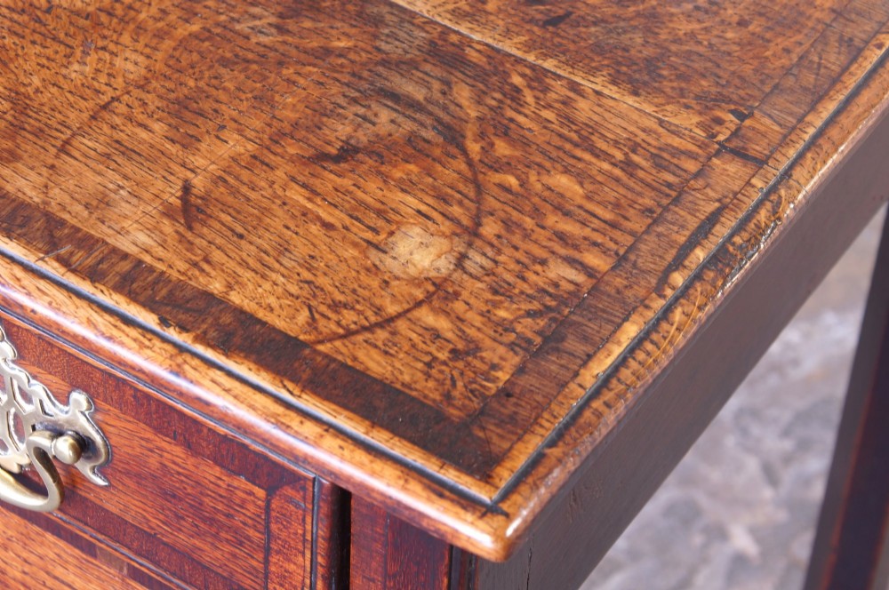 An 18th-century Georgian oak side table featuring a single drawer with decorative brass backplates and handles, set above a shaped apron and straight legs. View IV