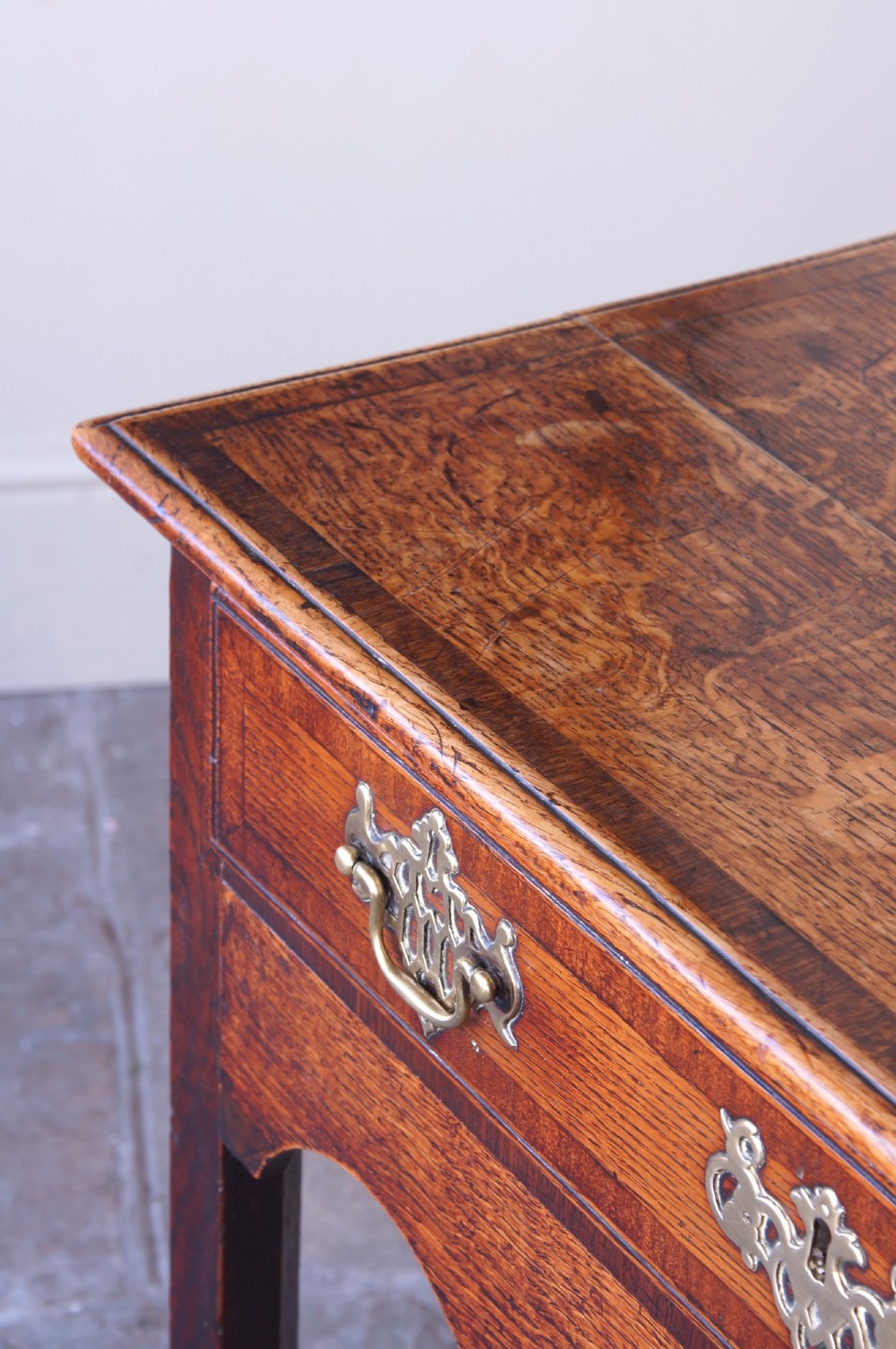 An 18th-century Georgian oak side table featuring a single drawer with decorative brass backplates and handles, set above a shaped apron and straight legs. View VI