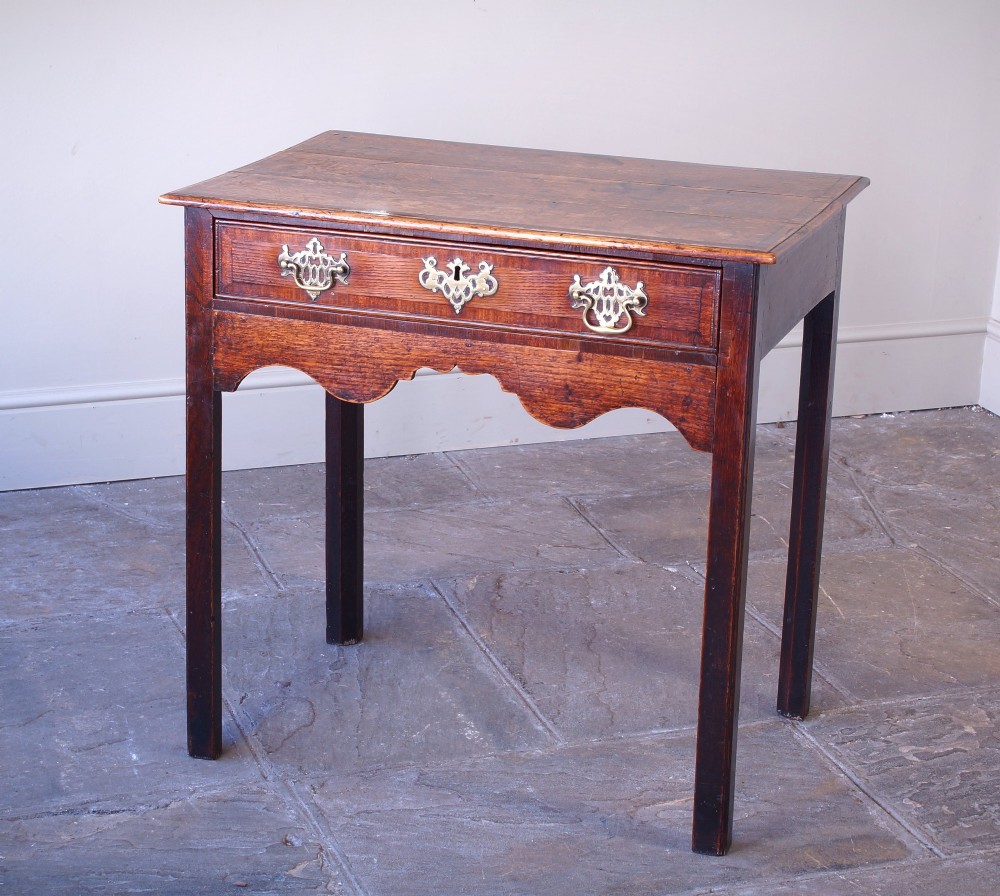 An 18th-century Georgian oak side table featuring a single drawer with decorative brass backplates and handles, set above a shaped apron and straight legs. View VII