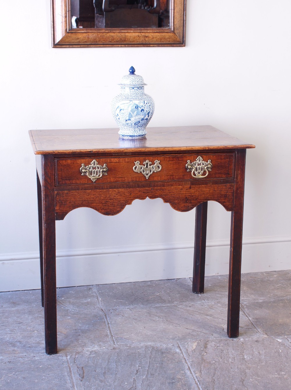 An 18th-century Georgian oak side table featuring a single drawer with decorative brass backplates and handles, set above a shaped apron and straight legs. View VIII