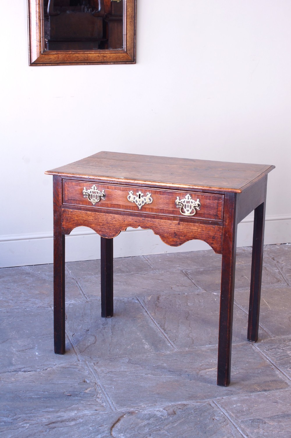 An 18th-century Georgian oak side table featuring a single drawer with decorative brass backplates and handles, set above a shaped apron and straight legs. View IX