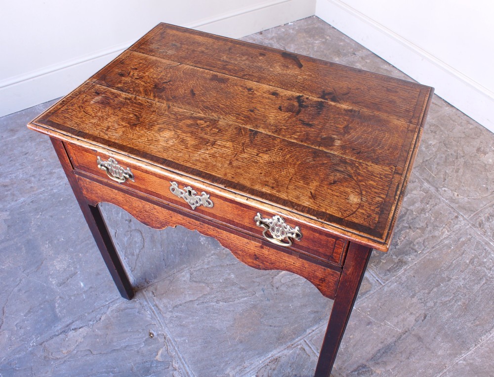 An 18th-century Georgian oak side table featuring a single drawer with decorative brass backplates and handles, set above a shaped apron and straight legs. View XI