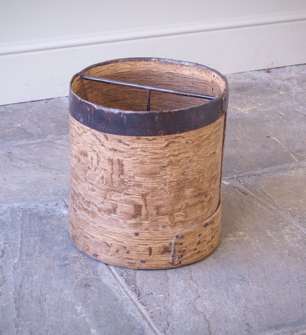 A cylindrical nineteenth-century French wooden grain measure with rustic iron banding, hand-riveted joints, and a central iron crossbar.