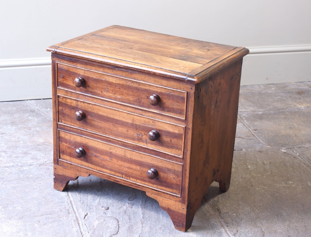 A Georgian plumwood close stool disguised as a small three-drawer chest with turned wooden knobs and bracket feet.