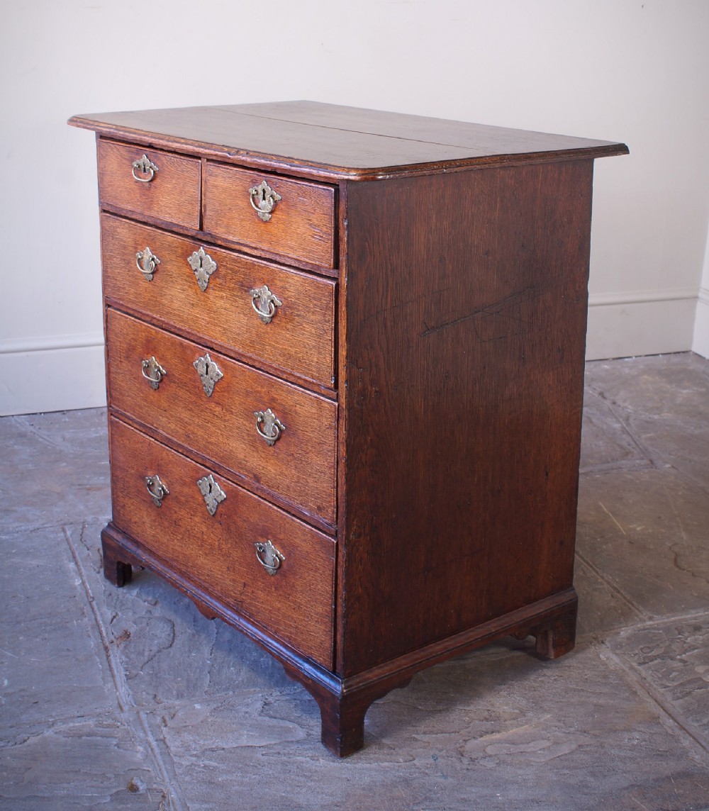 An early eighteenth-century oak chest of drawers featuring two short over three long drawers with brass drop handles and bracket feet. View IV