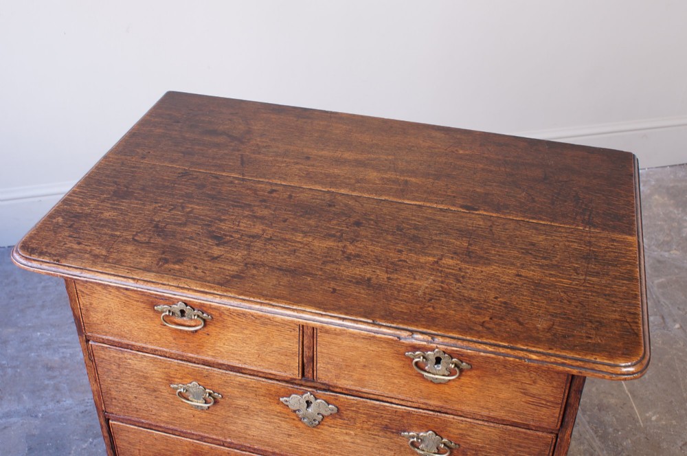 An early eighteenth-century oak chest of drawers featuring two short over three long drawers with brass drop handles and bracket feet. View V