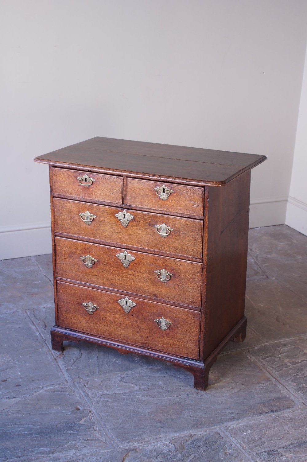 An early eighteenth-century oak chest of drawers featuring two short over three long drawers with brass drop handles and bracket feet. View VII