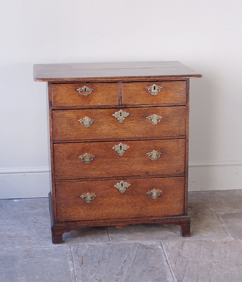 An early eighteenth-century oak chest of drawers featuring two short over three long drawers with brass drop handles and bracket feet. View IX