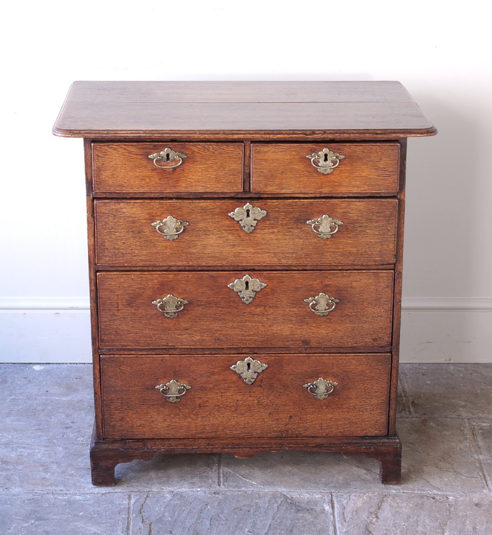 An early eighteenth-century oak chest of drawers featuring two short over three long drawers with brass drop handles and bracket feet. View X