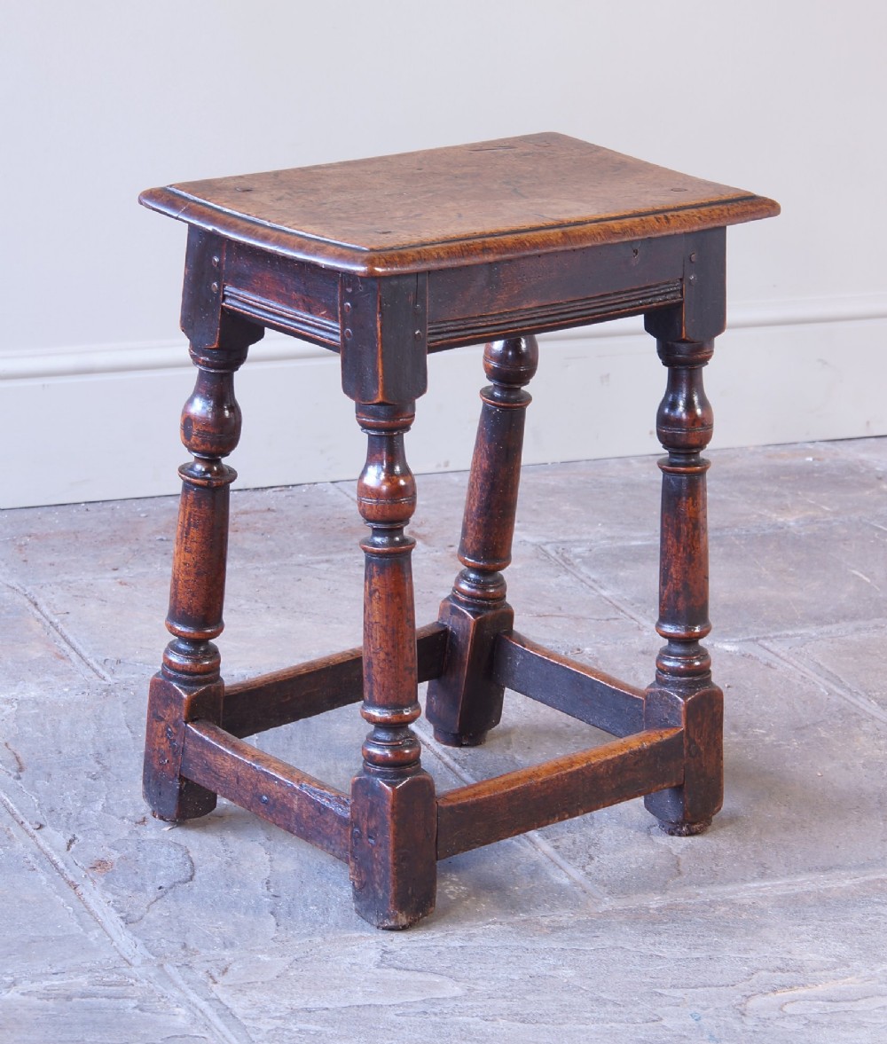 A 17th-century walnut joint stool featuring a rectangular moulded top, baluster turned legs, square pegged joinery, and a lower stretcher base with a dark patina. View IV