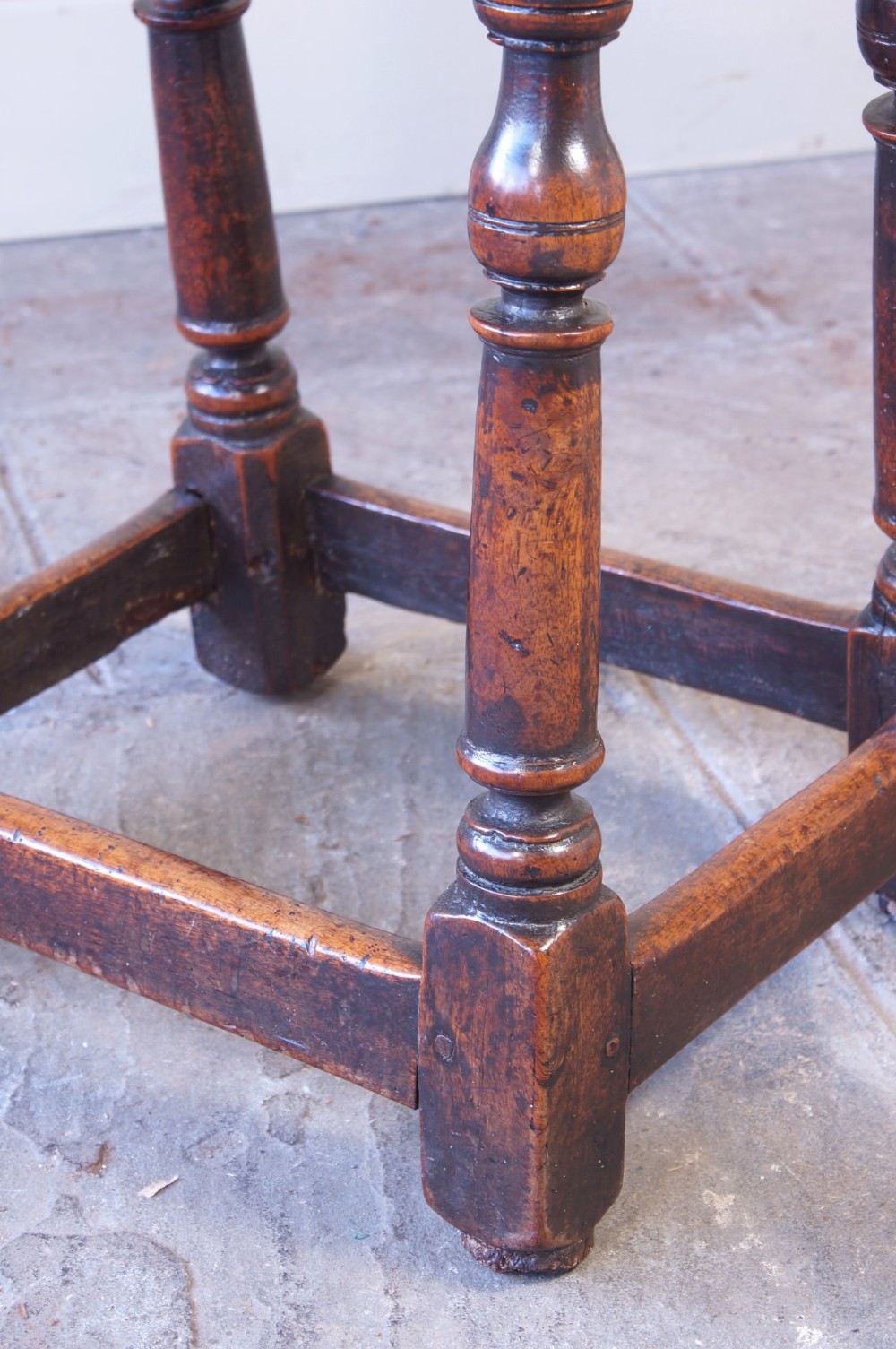 A 17th-century walnut joint stool featuring a rectangular moulded top, baluster turned legs, square pegged joinery, and a lower stretcher base with a dark patina. View VIII