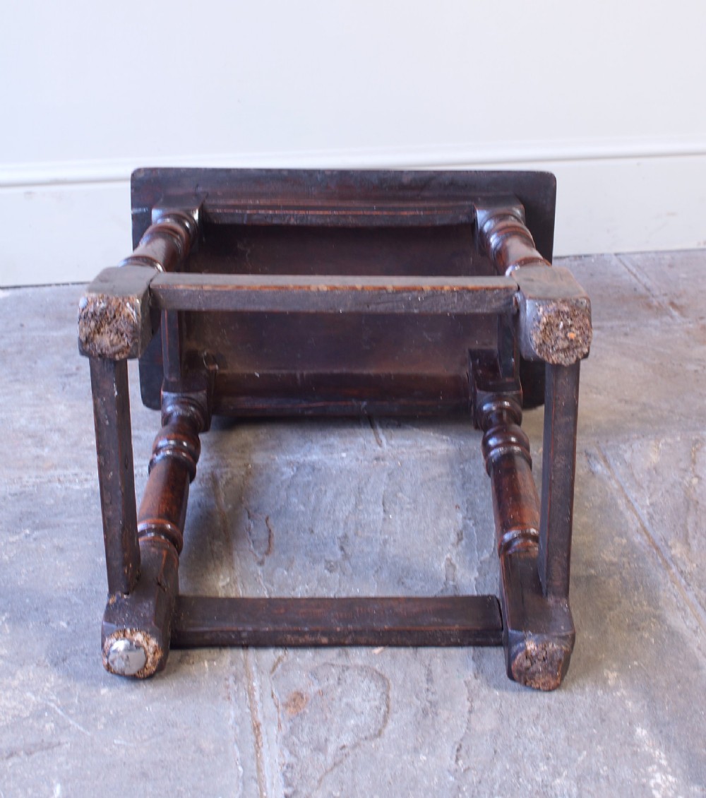 A 17th-century walnut joint stool featuring a rectangular moulded top, baluster turned legs, square pegged joinery, and a lower stretcher base with a dark patina. View XIII