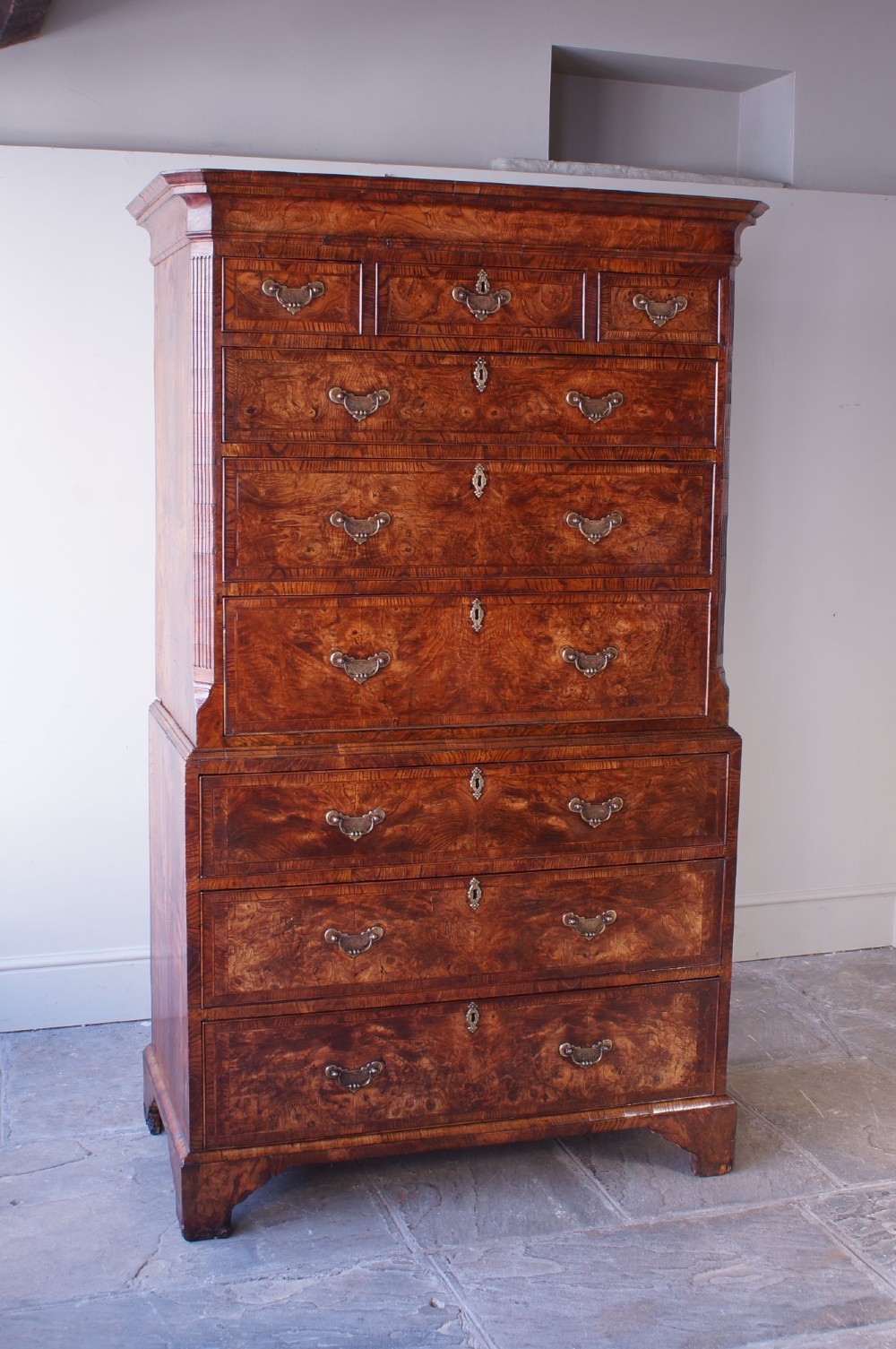An 18th-century chest on chest crafted from figured ash featuring multiple graduated drawers with brass drop handles and bracket feet. View IX