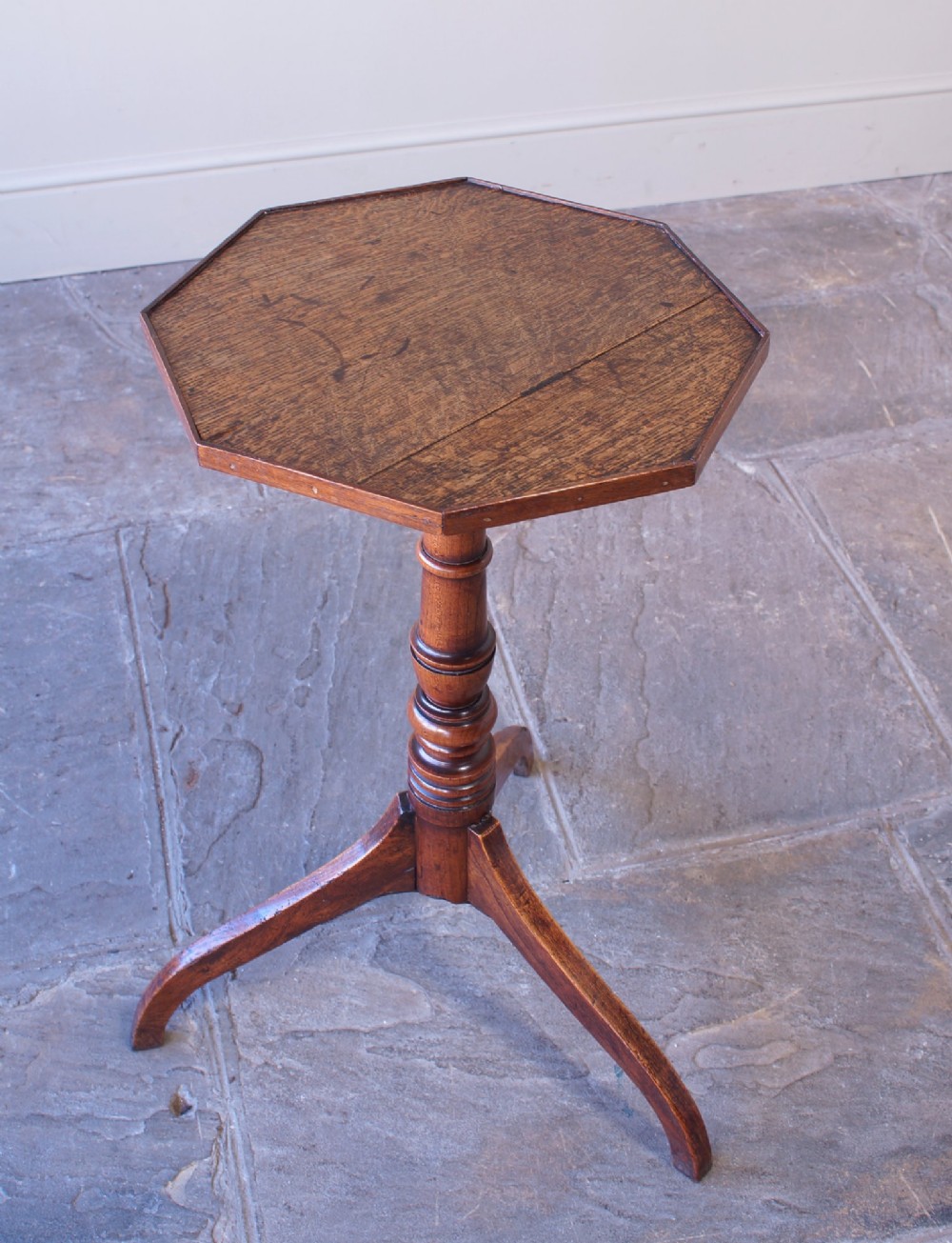 A Georgian oak and elm wine table featuring an octagonal top over a turned pedestal base with three down-swept tripod legs.