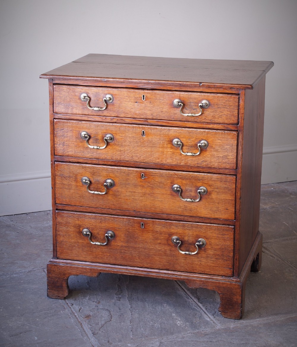 A small Georgian oak chest of drawers featuring four graduated drawers with brass swan-neck handles and bracket feet. View IV