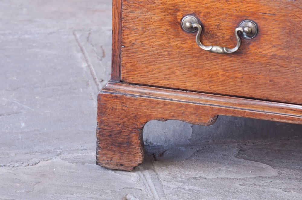 A small Georgian oak chest of drawers featuring four graduated drawers with brass swan-neck handles and bracket feet. View V