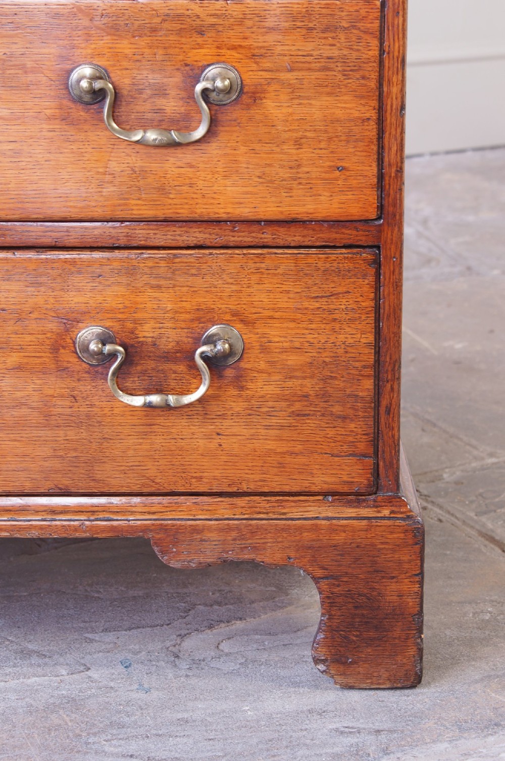 A small Georgian oak chest of drawers featuring four graduated drawers with brass swan-neck handles and bracket feet. View VII