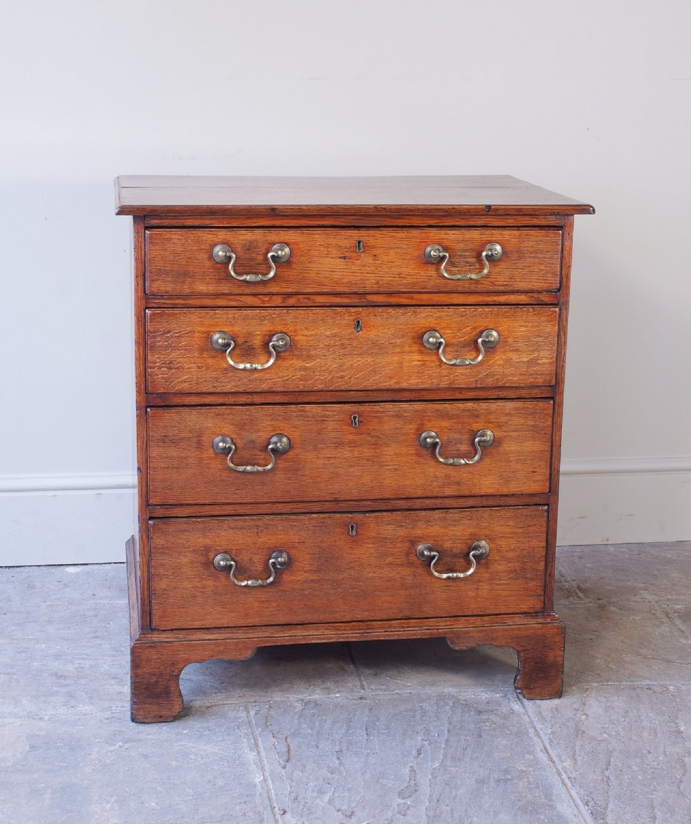 A small Georgian oak chest of drawers featuring four graduated drawers with brass swan-neck handles and bracket feet. View XIII